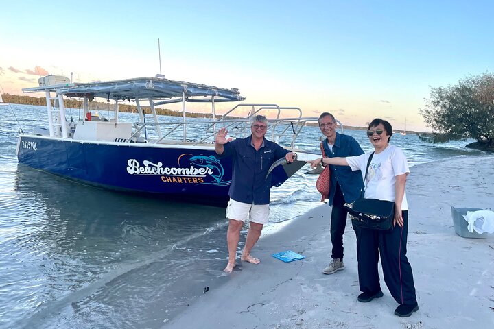 Three people beside a blue fishing boat at a riverside ramp
