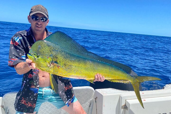 An angler holding a fish on a boat above blue ocean water