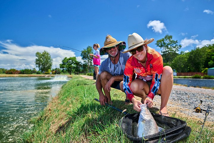 Two anglers with a fish on a grassy bank beside water
